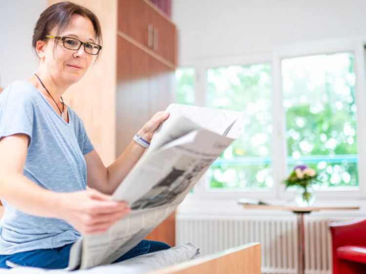 Patientin liest Zeitung in ihrem Zimmer