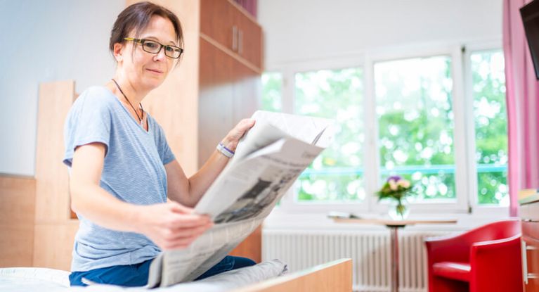 Patientin liest Zeitung in ihrem Zimmer