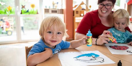 Zwei kleine Kinder malen Bilder mit einer Betreuerin