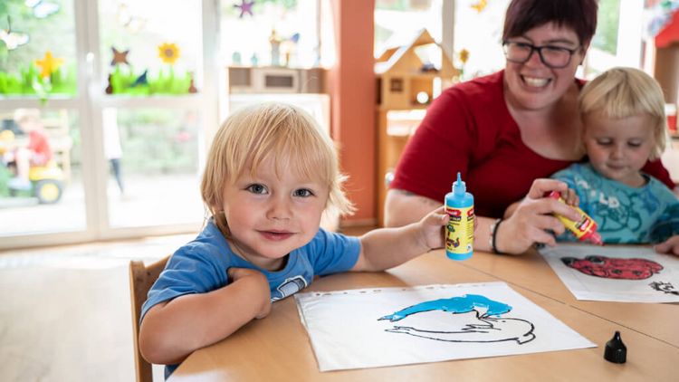 Zwei kleine Kinder malen Bilder mit einer Betreuerin