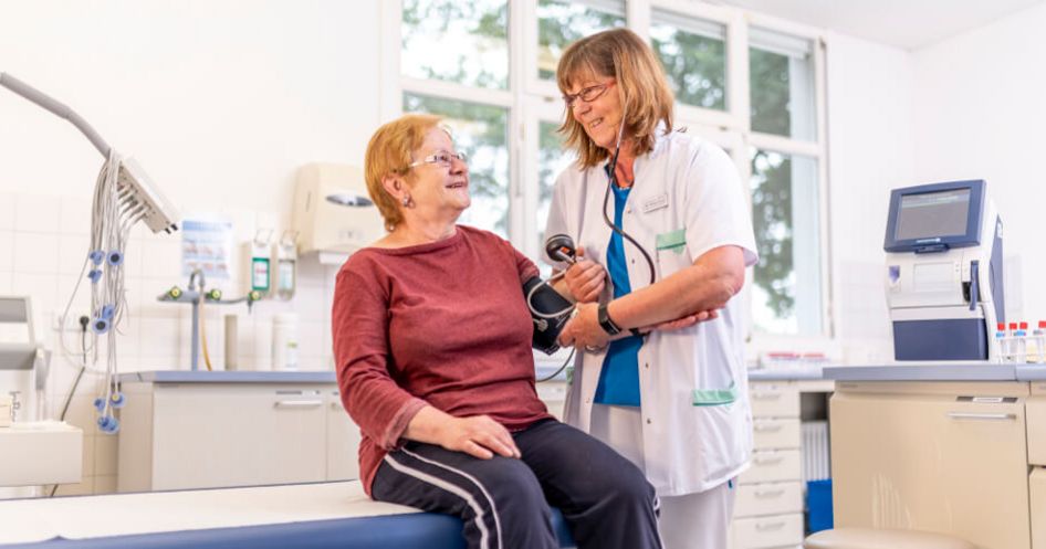 Pflegekraft misst Blutdruck bei einer älteren Patientin