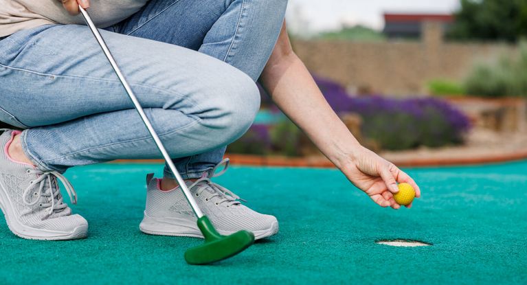 Frau kniet am Loch mit Fahne auf einem Golfplatz
