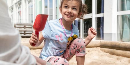 Kind spielt mit roter Schaufel im Sandkasten