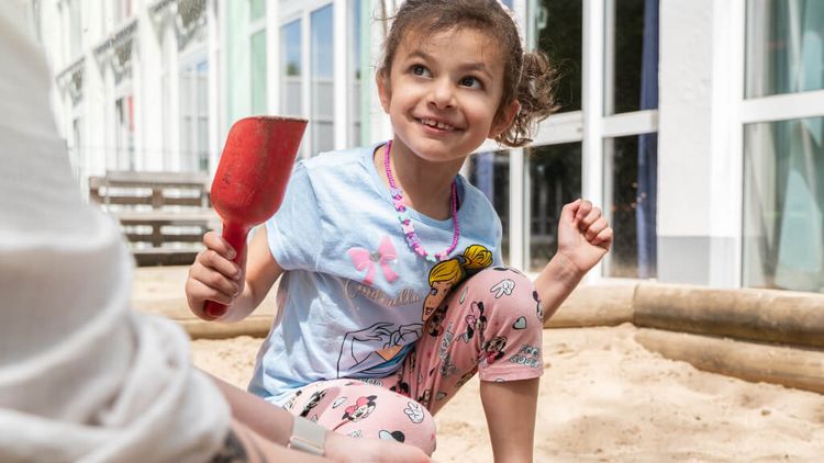Kind spielt mit roter Schaufel im Sandkasten
