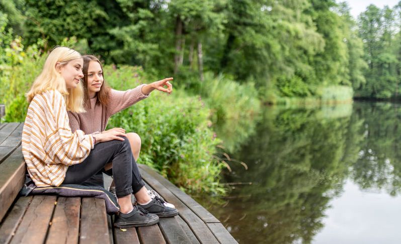 Zwei junge Frauen sitzen auf einem Steg am See