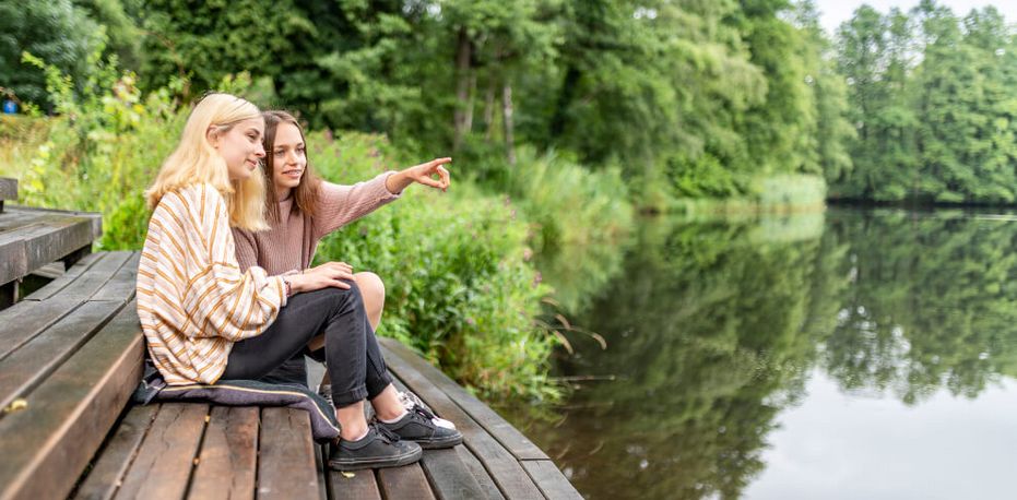 Zwei junge Frauen sitzen auf einem Steg am See