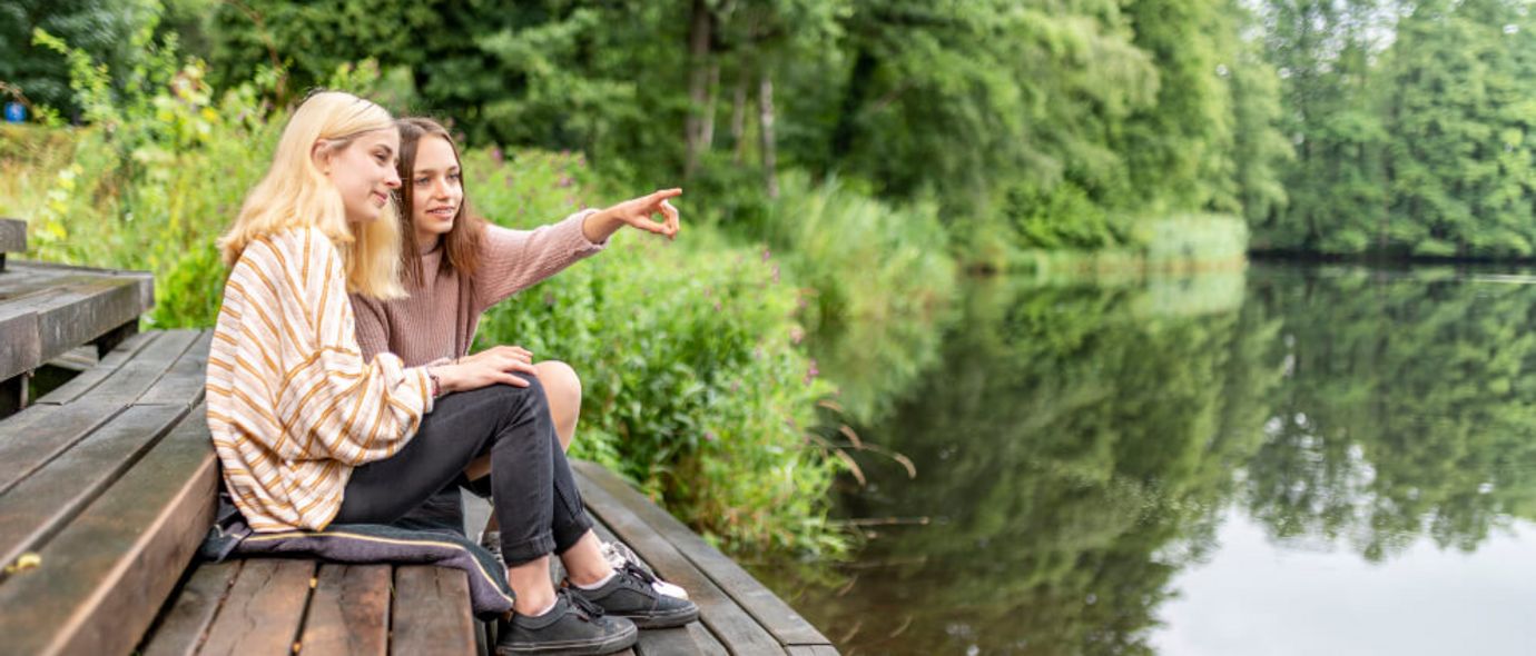 Zwei junge Frauen sitzen auf einem Steg am See
