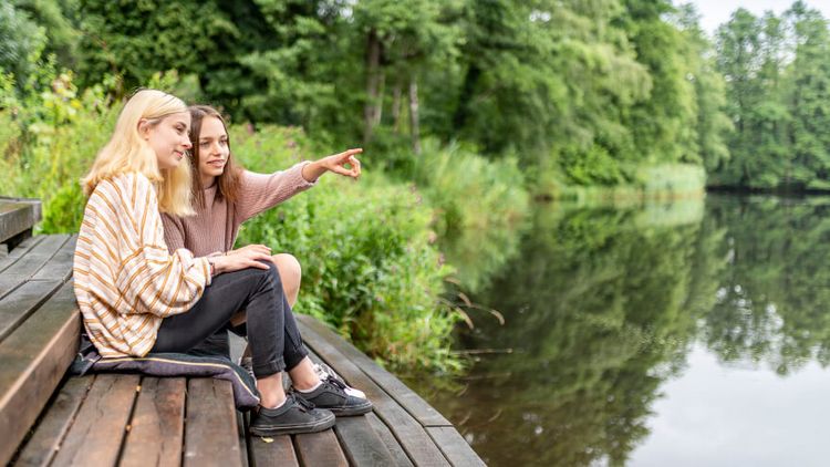 Zwei junge Frauen sitzen auf einem Steg am See